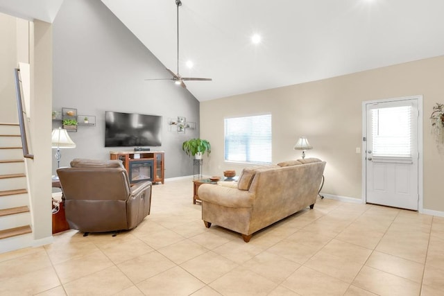 living area with stairway, light tile patterned floors, baseboards, high vaulted ceiling, and ceiling fan