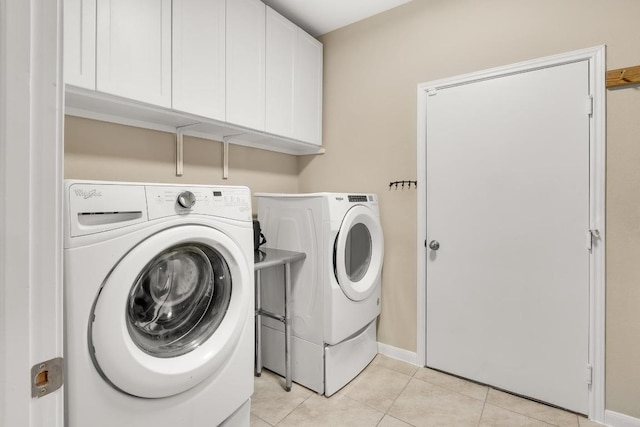 laundry area featuring light tile patterned floors, baseboards, cabinet space, and washing machine and clothes dryer