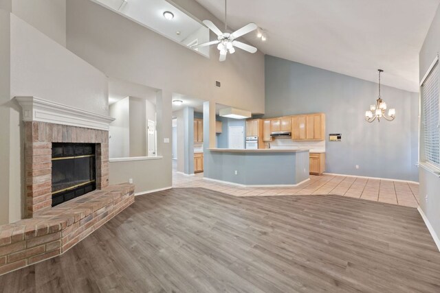 unfurnished living room featuring ceiling fan with notable chandelier, visible vents, baseboards, light wood-type flooring, and a brick fireplace