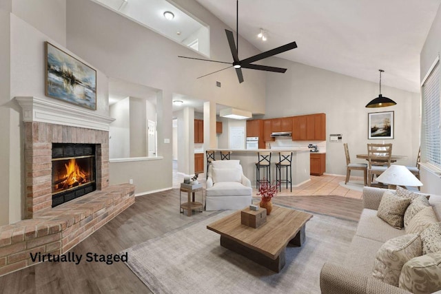 living room featuring baseboards, light wood-style floors, ceiling fan, vaulted ceiling, and a brick fireplace