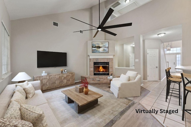 living room featuring light tile patterned floors, high vaulted ceiling, a fireplace, visible vents, and a ceiling fan