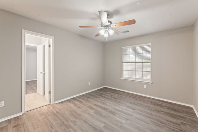 spare room featuring ceiling fan, visible vents, baseboards, and wood finished floors