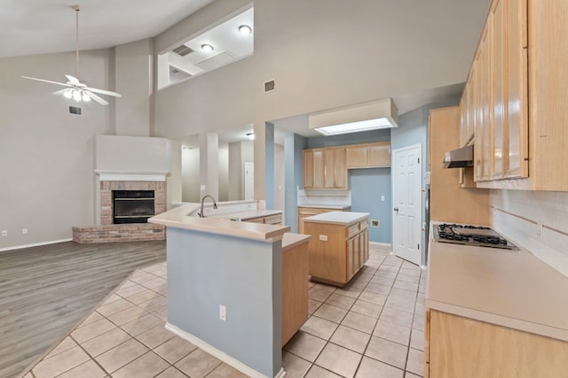 kitchen with stainless steel gas stovetop, open floor plan, light brown cabinets, a kitchen island, and under cabinet range hood