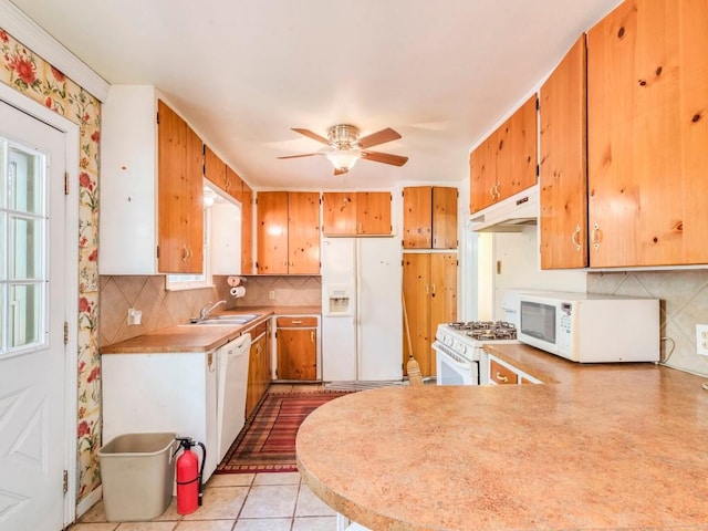 kitchen with under cabinet range hood, a peninsula, white appliances, light countertops, and decorative backsplash