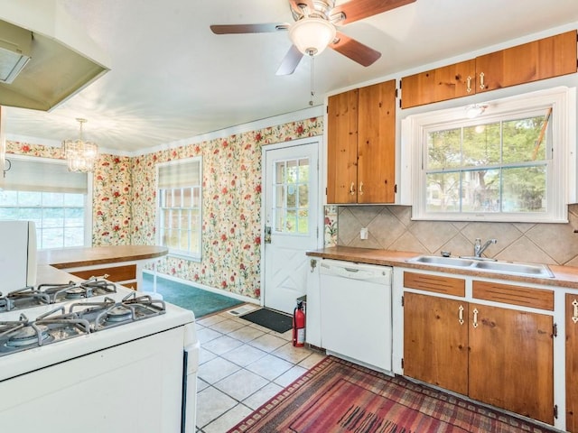 kitchen with brown cabinets, light countertops, a sink, white appliances, and wallpapered walls