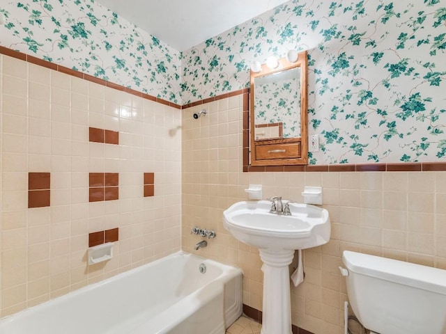 bathroom featuring a wainscoted wall, tile walls, shower / bathing tub combination, toilet, and wallpapered walls