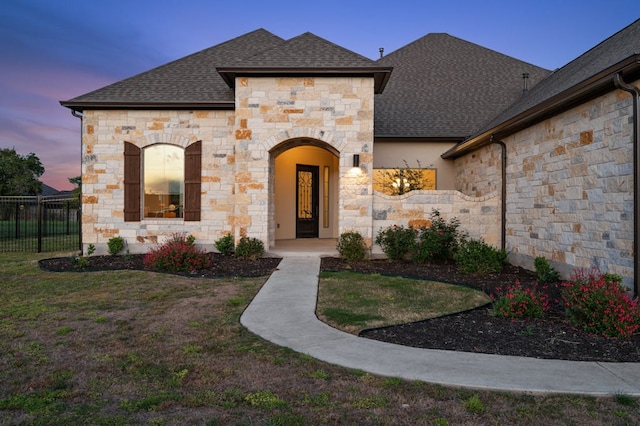 french provincial home with a shingled roof, a front yard, and fence