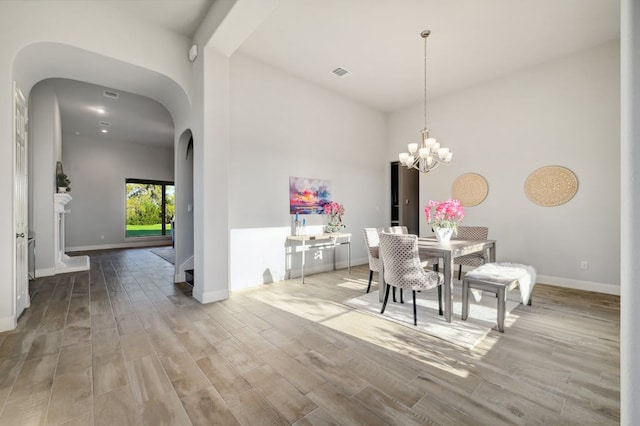 dining area featuring baseboards, visible vents, arched walkways, wood finished floors, and an inviting chandelier