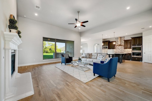 living room with recessed lighting, visible vents, baseboards, light wood-type flooring, and a glass covered fireplace