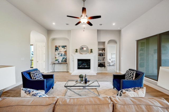 living room with wood finished floors, a glass covered fireplace, visible vents, and built in features