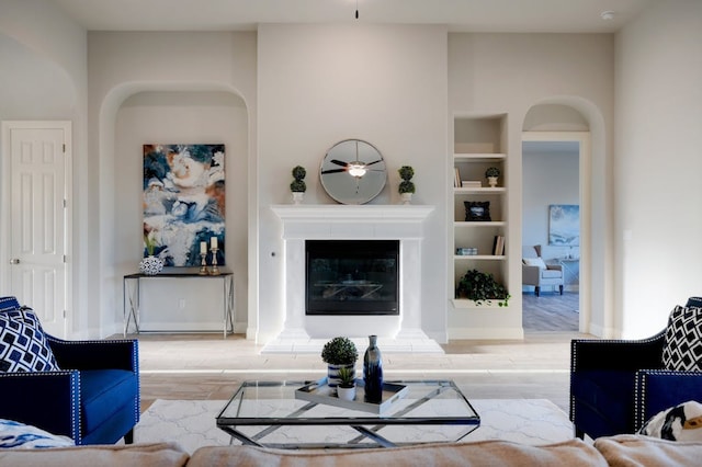 living room featuring built in features, arched walkways, wood finished floors, and a glass covered fireplace