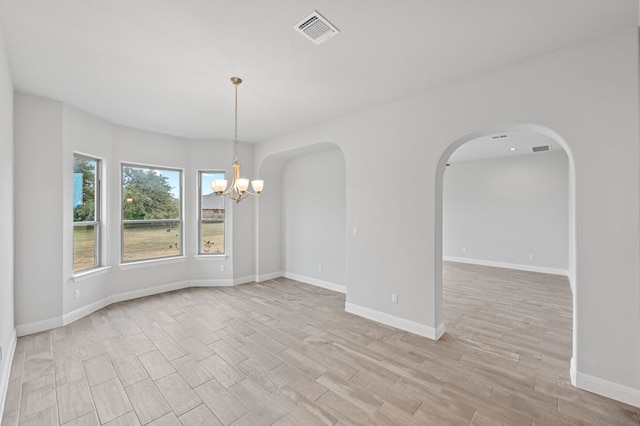 empty room featuring arched walkways, visible vents, light wood-style floors, a chandelier, and baseboards