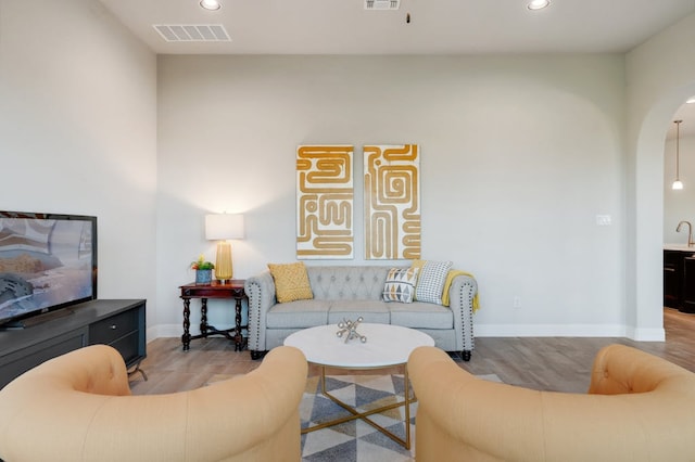 living room with arched walkways, wood finished floors, visible vents, and recessed lighting