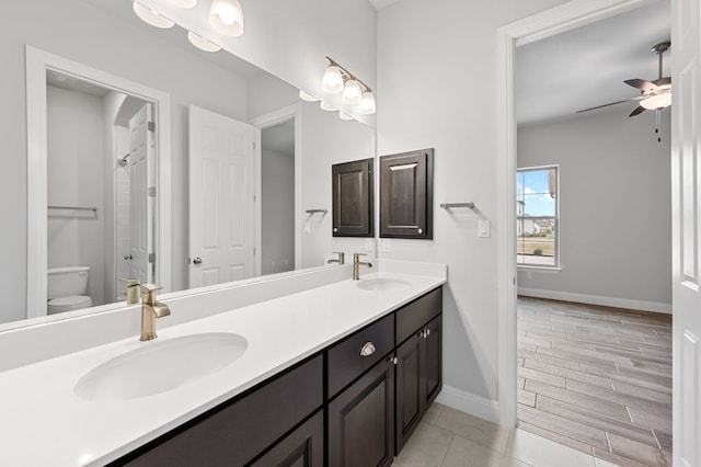 bathroom featuring ceiling fan, double vanity, a sink, and baseboards