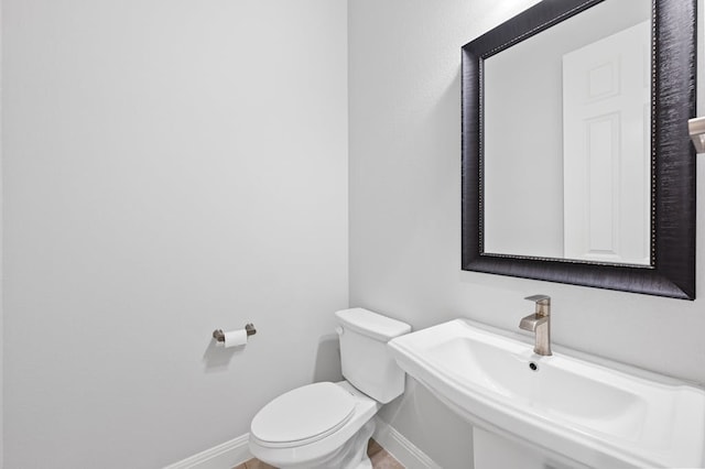 half bathroom with toilet, baseboards, and a sink