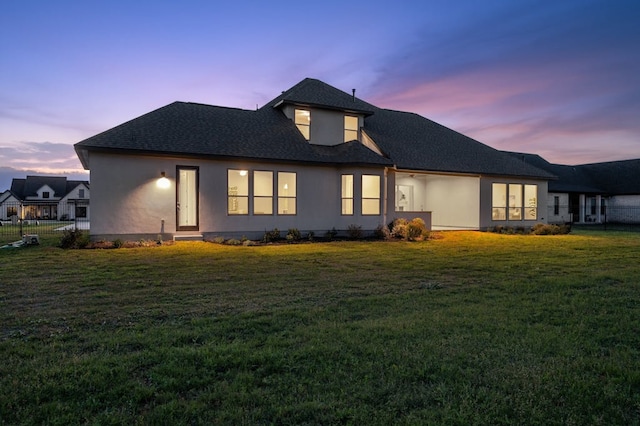 exterior space featuring roof with shingles, a lawn, fence, and stucco siding