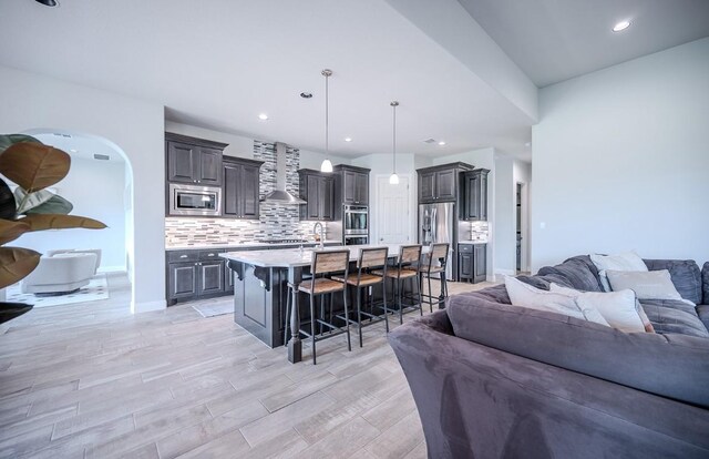 227 Dally Ct, Dripping Springs, TX 78620 - kitchen featuring open floor plan, stainless steel appliances, wall chimney range hood, a kitchen breakfast bar, and recessed lighting