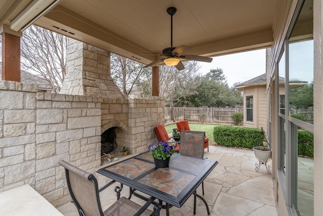 view of patio / terrace with a ceiling fan, an outdoor stone fireplace, fence, and outdoor dining area