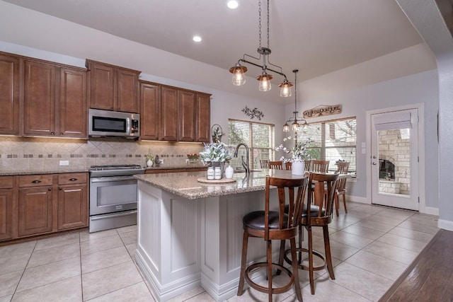 kitchen featuring light stone counters, a breakfast bar area, stainless steel appliances, decorative backsplash, and a kitchen island with sink