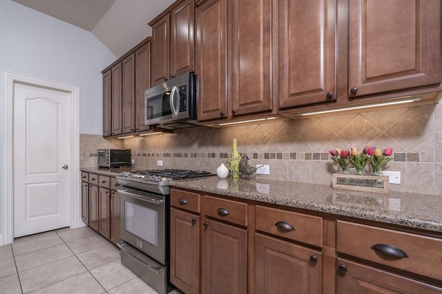 kitchen featuring light tile patterned floors, light stone countertops, vaulted ceiling, stainless steel appliances, and backsplash