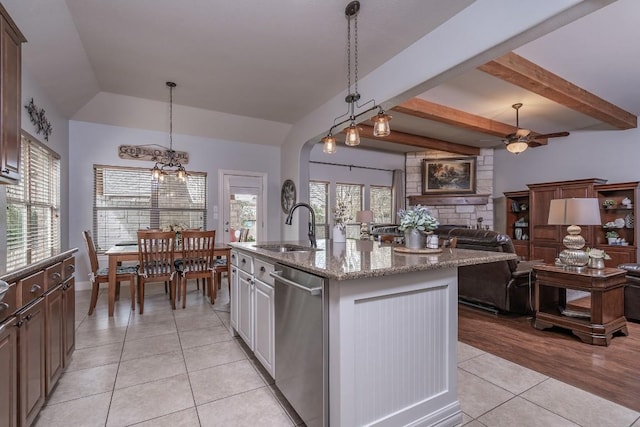 kitchen featuring light stone counters, a center island with sink, stainless steel dishwasher, light tile patterned flooring, and a sink