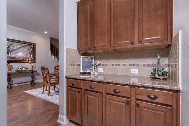 kitchen featuring decorative backsplash, ornamental molding, brown cabinets, dark wood-type flooring, and light stone countertops