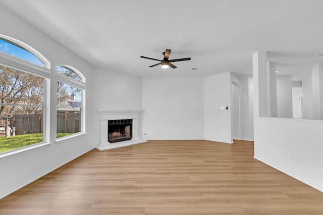 unfurnished living room featuring light wood-style floors, a fireplace with raised hearth, and ceiling fan