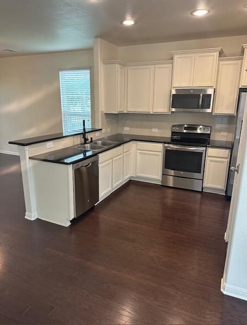 kitchen featuring dark wood-style flooring, a sink, white cabinetry, appliances with stainless steel finishes, and dark countertops