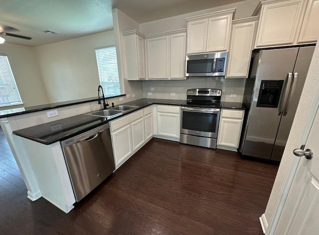 kitchen with a peninsula, dark wood-style floors, appliances with stainless steel finishes, and a sink