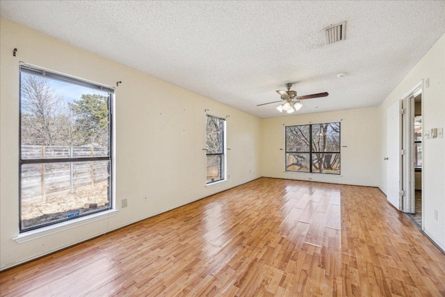 spare room featuring light wood-type flooring, visible vents, ceiling fan, and a textured ceiling