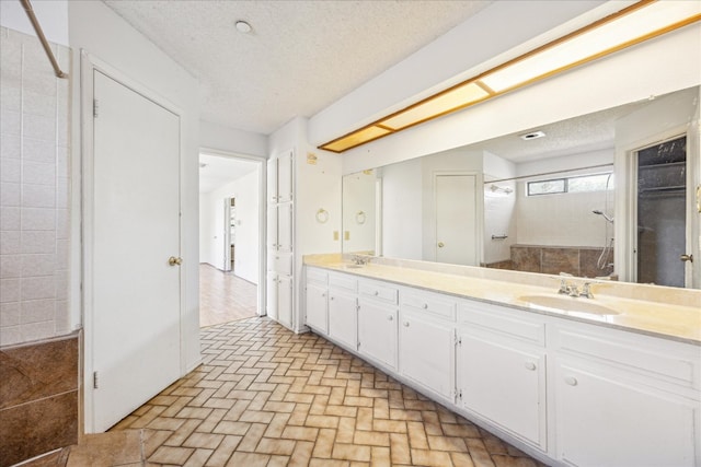 bathroom with double vanity, brick floor, a tile shower, a textured ceiling, and a sink