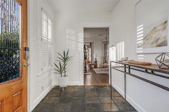 foyer entrance featuring a chandelier, stone finish floor, and baseboards