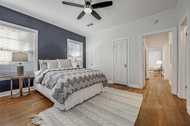 bedroom with baseboards, visible vents, crown molding, and light wood finished floors