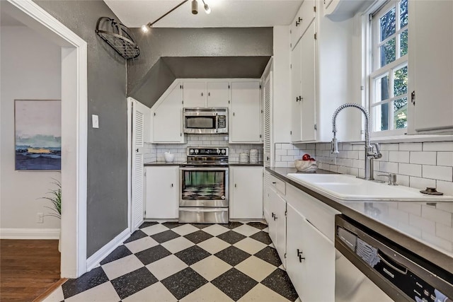 kitchen with white cabinets, a sink, stainless steel appliances, light floors, and backsplash