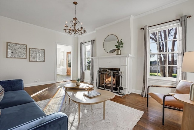 living room featuring a warm lit fireplace, baseboards, wood finished floors, and crown molding