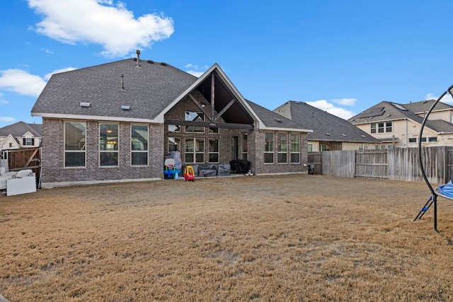 rear view of house with a yard, a fenced backyard, roof with shingles, and brick siding