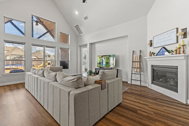 living area featuring dark wood-type flooring, a glass covered fireplace, and visible vents