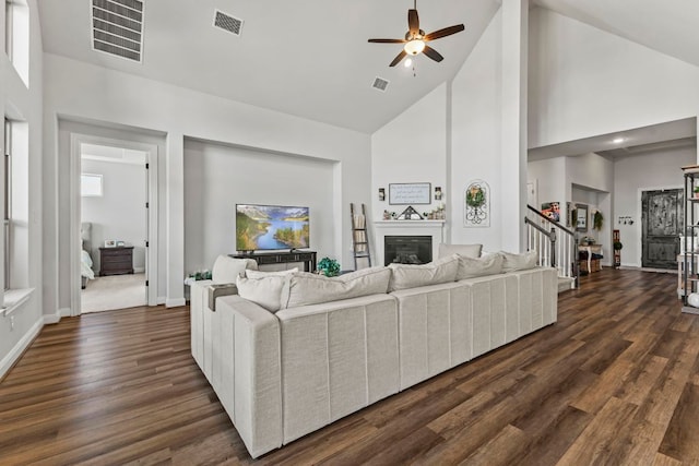 living area featuring dark wood-type flooring, stairway, a glass covered fireplace, and visible vents