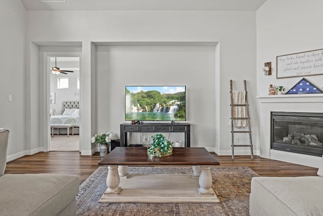 living room with ceiling fan, baseboards, wood finished floors, and a glass covered fireplace