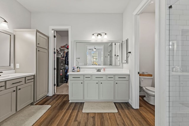 full bath with toilet, two vanities, wood finished floors, a tile shower, and a sink