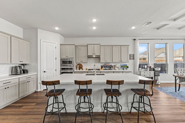 kitchen featuring stainless steel appliances, a kitchen island with sink, visible vents, and dark wood-style floors