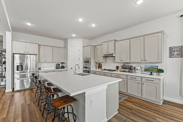 kitchen with a breakfast bar, a center island with sink, stainless steel appliances, dark wood-type flooring, and a sink