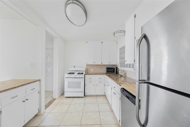 kitchen featuring light tile patterned floors, decorative backsplash, stainless steel appliances, white cabinetry, and a sink