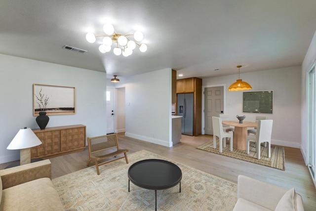 living area featuring an inviting chandelier, light wood-type flooring, visible vents, and baseboards