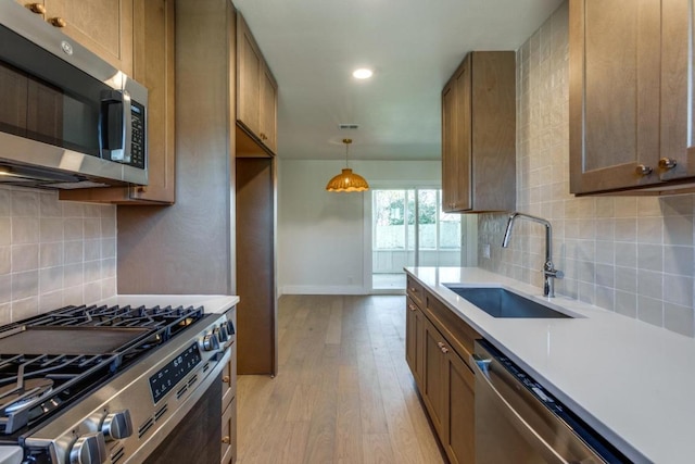 kitchen with a sink, stainless steel appliances, light countertops, light wood-type flooring, and backsplash