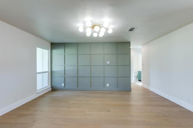 unfurnished room with light wood-type flooring, visible vents, a notable chandelier, and baseboards