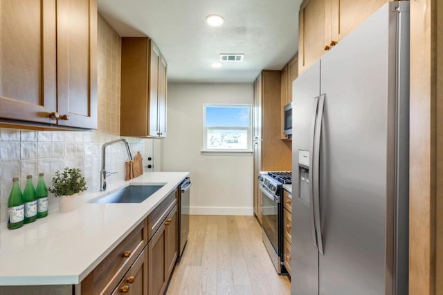 kitchen with stainless steel appliances, tasteful backsplash, visible vents, light wood-style floors, and a sink