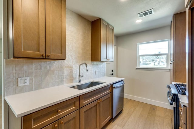 kitchen with visible vents, a sink, stainless steel appliances, light wood-type flooring, and backsplash