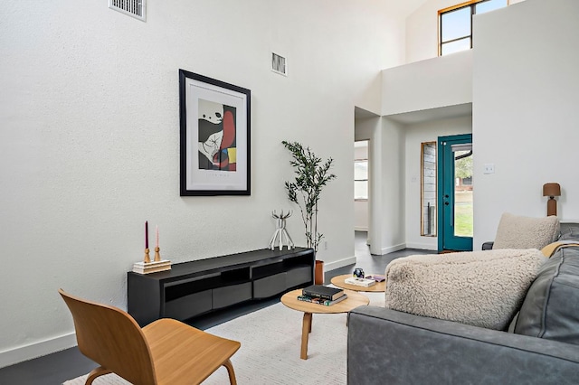 living area featuring baseboards, a high ceiling, and visible vents