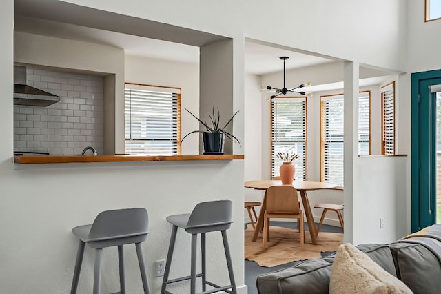 kitchen with wall chimney range hood, a breakfast bar, and a notable chandelier